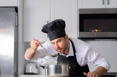 Profesyonel üniformalı modern şef. Kaşıkla tencereye çorba karıştıran erkek aşçının eline yakın plan. Yemek pişirme, aşçılık ve insan konsepti - erkek aşçı tencereli veya tencereli.