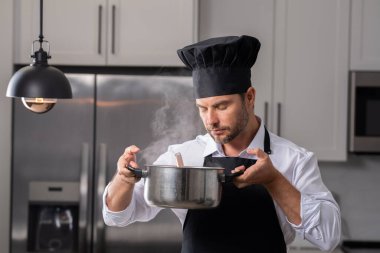 Profesyonel üniformalı modern şef. Kaşıkla tencereye çorba karıştıran erkek aşçının eline yakın plan. Yemek pişirme, aşçılık ve insan konsepti - erkek aşçı tencereli veya tencereli.