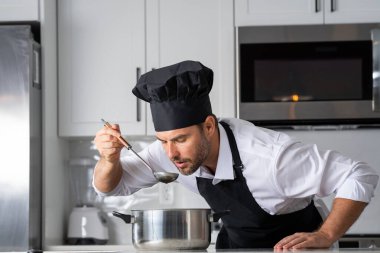 Profesyonel üniformalı modern şef. Kaşıkla tencereye çorba karıştıran erkek aşçının eline yakın plan. Yemek pişirme, aşçılık ve insan konsepti - erkek aşçı tencereli veya tencereli.