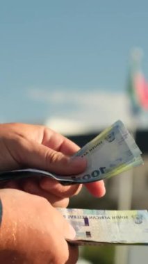 Adam Güney Afrika 'nın paralarını sayıyor. Güney Afrika bayrağının arka planında beyaz gömlek ve takım elbiseli Avrupalı bir işadamının ellerine yakın plan çekilmiş.