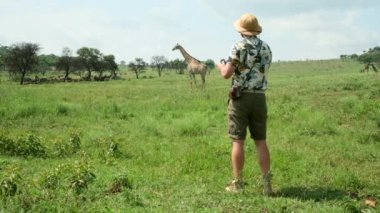 Afrika 'da safaride turist fotoğrafçısı. Safari Macerası sırasında Zürafa Fotoğrafları Çeken Turist. Adam vahşi hayatın fotoğrafını çekiyor. Savanadaki bir safarinin altın gündoğumu sırasında.