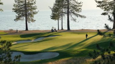 Gün batımında güzel bir golf sahası. Gün batımında yemyeşil çim yolu, yeşil ve kum deposu üzerindeki panoramik manzara. Golf sahası sporu, yeşil çimenler ve golf arabasındaki ağaçlar.