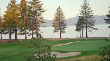 Gün batımında güzel bir golf sahası. Gün batımında yemyeşil çim yolu, yeşil ve kum deposu üzerindeki panoramik manzara. Golf sahası sporu, yeşil çimenler ve golf arabasındaki ağaçlar.