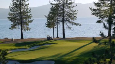 Gün batımında güzel bir golf sahası. Gün batımında yemyeşil çim yolu, yeşil ve kum deposu üzerindeki panoramik manzara. Golf sahası sporu, yeşil çimenler ve golf arabasındaki ağaçlar.