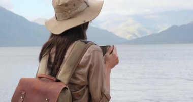 Sırt çantalı kadın yürüyüşçü dağlarda dinlenirken sıcak çay içiyor. Yürüyüşçü dağlardaki bir gölün yakınında sıcak bir içecek içer. Amerikalı bir turist Amerikan dağlarında tek başına yürüyüş yapıyor.