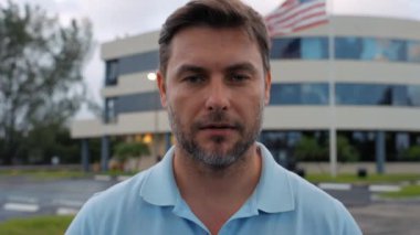 Amerikalı bir adam, Amerikan bayrağının arka planına karşı kameraya bakıyor. Tişörtlü kibar ve kendinden emin bir adam New York 'ta kameraya bakar ve gülümser. Amerika 'da Amerikan bayrağı taşıyan bir adam 