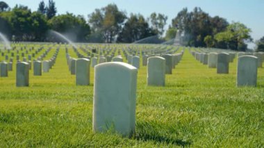 Amerikan savaş mezarlığı anma günü. Sunny Day 'in altında mavi gökyüzüyle ABD Bayrakları. Amerikan savaş mezarlığı, çiçeklerle süslenmiş, askerlere dokunaklı bir övgü yansıtıyor.