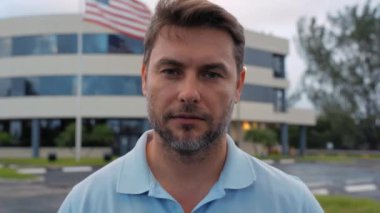 Mutlu adam dışarıda gülümsüyor. Şehirdeki sokaktaki mutlu genç adamın portresi. Neşeli, neşeli, yakışıklı adam kameraya bakıyor. Özgürlük mutluluğu tasasız mutlu insanlar konsepti. Amerikan bayrağı taşıyan adam