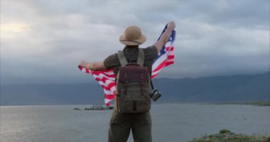 Amerikan bayrağı tutan adam. Vatansever bayram. Gün batımında buğday tarlasında Amerikan bayrağıyla gezen vatansever bir genç. Bağımsızlık Günü, 4 Temmuz. Macera ve seyahat dağlık bölgede.