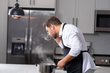 Profesyonel üniformalı modern şef. Kaşıkla tencereye çorba karıştıran erkek aşçının eline yakın plan. Yemek pişirme, aşçılık ve insan konsepti - erkek aşçı tencereli veya tencereli.