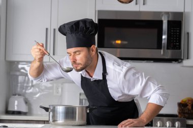 Profesyonel üniformalı modern şef. Kaşıkla tencereye çorba karıştıran erkek aşçının eline yakın plan. Yemek pişirme, aşçılık ve insan konsepti - erkek aşçı tencereli veya tencereli.