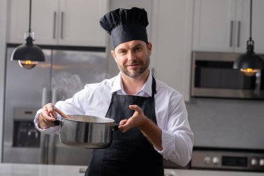 Profesyonel üniformalı modern şef. Kaşıkla tencereye çorba karıştıran erkek aşçının eline yakın plan. Yemek pişirme, aşçılık ve insan konsepti - erkek aşçı tencereli veya tencereli.