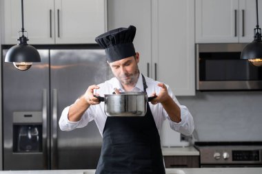 Profesyonel üniformalı modern şef. Kaşıkla tencereye çorba karıştıran erkek aşçının eline yakın plan. Yemek pişirme, aşçılık ve insan konsepti - erkek aşçı tencereli veya tencereli.