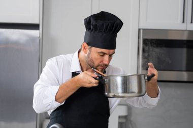 Profesyonel üniformalı modern şef. Kaşıkla tencereye çorba karıştıran erkek aşçının eline yakın plan. Yemek pişirme, aşçılık ve insan konsepti - erkek aşçı tencereli veya tencereli.