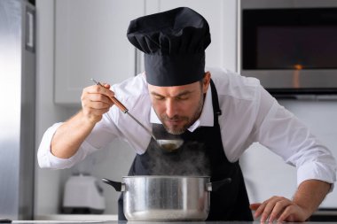 Profesyonel üniformalı modern şef. Kaşıkla tencereye çorba karıştıran erkek aşçının eline yakın plan. Yemek pişirme, aşçılık ve insan konsepti - erkek aşçı tencereli veya tencereli.