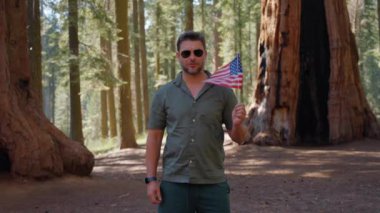 Açık havada Amerikan bayrağı. Ormanda mavi bulutlu gökyüzüne karşı ulusal bayrak taşıyan bir adam. 4 Temmuz Bağımsızlık Günü. Anma ve Gaziler Günü. ABD 'nin ulusal bayrağı.