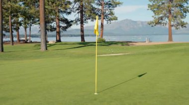 Golf sopası ve top çimlerde. Golf topu yeşilde. Top bardakta. Yeşil çimlerin üzerinde golf sopası ve topunun yakın çekimi gün batımında sakin bir golf sahasının özünü yakalıyor.