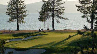 Gün batımında güzel bir golf sahası. Gün batımında yemyeşil çim yolu, yeşil ve kum deposu üzerindeki panoramik manzara. Golf sahası sporu, yeşil çimenler ve golf arabasındaki ağaçlar.