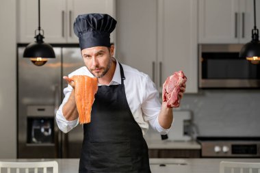 Restorandaki profesyonel mutfakta duran yakışıklı şef et, somon ve peynir sebzelerinden oluşan bir yemek hazırlıyor. Mutfaktaki şef elinde et ve balık tutuyor, konsept balık ya da et.