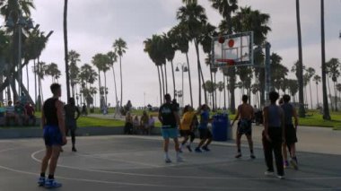 Los Angeles kortunda sokak basketbolcusu. Güneşin doğuşunda basketbol oynuyor. Atletik siyahi adam sahada sırt topu yeteneğini gösteriyor. 25 Eylül 2024 'te sokak basketbolu oynayan arkadaşlar 