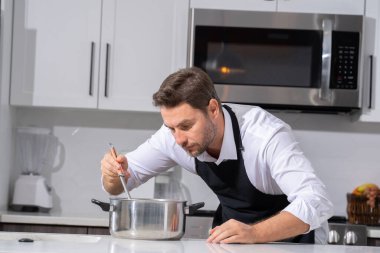 Profesyonel üniformalı modern şef. Kaşıkla tencereye çorba karıştıran erkek aşçının eline yakın plan. Yemek pişirme, aşçılık ve insan konsepti - erkek aşçı tencereli veya tencereli.
