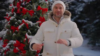 Noel ağacının yanında kışlık ceketli bir adam elleriyle bir kalp gösteriyor. Adam Aşkı Göstermek İçin Elleriyle Kalp Şekli Yapıyor. Adam elleriyle kalp sembolü yapıyor. Bir adam ve Noel neşesi