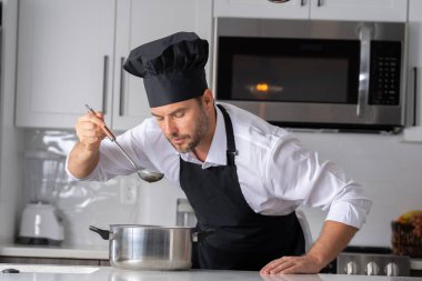 Profesyonel üniformalı modern şef. Kaşıkla tencereye çorba karıştıran erkek aşçının eline yakın plan. Yemek pişirme, aşçılık ve insan konsepti - erkek aşçı tencereli veya tencereli.