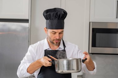 Profesyonel üniformalı modern şef. Kaşıkla tencereye çorba karıştıran erkek aşçının eline yakın plan. Yemek pişirme, aşçılık ve insan konsepti - erkek aşçı tencereli veya tencereli.