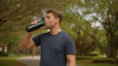 Açık hava egzersizi, antrenman ya da iyileşme maratonu için koşucu ve içme suyu. Adam çok çalıştıktan sonra içiyor. Sportif genç adam protein kokteyli içiyor, parkta eğitim görüyor.