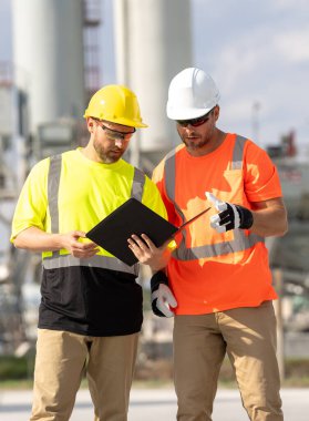 Kimya endüstrisi fabrikası. Rafineride çalışan işçiler. Boruları ve makineleri var. Demir şapka mühendisi petrol rafinerisi yakınlarında tablet kullanıyor. Petrokimya fabrikasındaki inşaat mühendisleri.