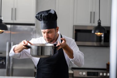 Profesyonel üniformalı modern şef. Kaşıkla tencereye çorba karıştıran erkek aşçının eline yakın plan. Yemek pişirme, aşçılık ve insan konsepti - erkek aşçı tencereli veya tencereli.