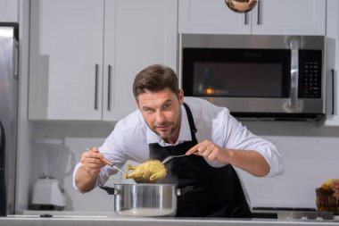 Profesyonel üniformalı modern şef. Kaşıkla tencereye çorba karıştıran erkek aşçının eline yakın plan. Yemek pişirme, aşçılık ve insan konsepti - erkek aşçı tencereli veya tencereli.