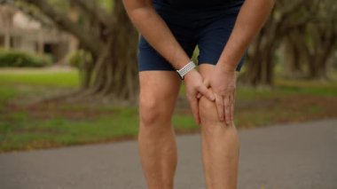 Kendini işine adamış bir koşucu, güzel yeşil bir ortamda koşarken dizini tutarak huzursuzluk içinde somurtuyor.