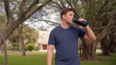 Açık hava egzersizi, antrenman ya da iyileşme maratonu için koşucu ve içme suyu. Adam çok çalıştıktan sonra içiyor. Sportif genç adam protein kokteyli içiyor, parkta eğitim görüyor.