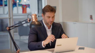 Olgun iş adamı, modern ofiste dizüstü bilgisayarla oturarak gözlüğü dijital ekrana odaklayacak şekilde ayarlar. Çalışma konsantrasyonu, iş veri analizi ve çevrimiçi iletişim kavramı. 