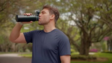 Atletik bir adam sakin bir sokakta sabah koşusundan sonra tekrar kullanılabilir bir spor şişesinden su içer. Sağlıklı yaşam tarzı, susuzluk, zindelik iyileşmesi ve doğadaki ekolojik bilinç alışkanlıkları üzerinde duruluyor..