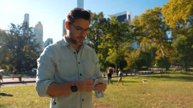 Sakallı, sıradan tişörtlü ve akıllı bir adam yeşil bir parka odaklanmışken bir yığın parayı sayıyor. Sahne mali kontrol, kişisel zenginlik ve düşünceli para yönetimini yansıtıyor..