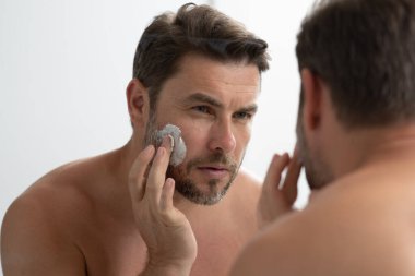 Banyoda yüz kremi süren yakışıklı bir adam. Yüz kreminden sonra tatmin olmuş genç bir adamın yakından güzel portresi. Çekici esmer adam tenine dokunuyor. Erkek kozmetik ve güzellik konsepti