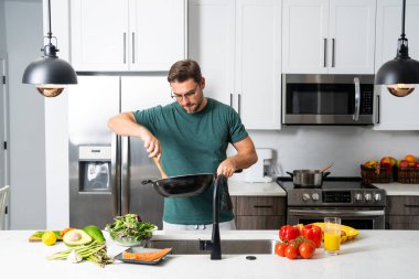 Erkek aşçı ev mutfağında Asya usulü sağlıklı yemek hazırlıyor. Avokado, yeşil salata, sebze ve taze otlarla yemek pişirmek. Diyet, sağlık yaşam tarzı, organik beslenme ve ev yapımı yemek kavramı.