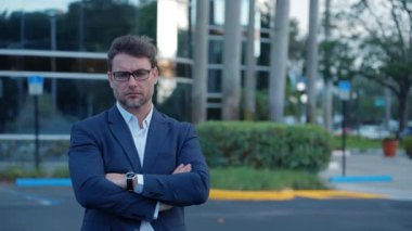 Kurumsal lider kollarını kavuşturmuş, güven ve otorite yansıtıyor. Takım elbiseli yetişkin bir adam ofis binası yakınlarında yönetici kılığına girmiş. Kentsel zemin liderlik ve strateji öneriyor