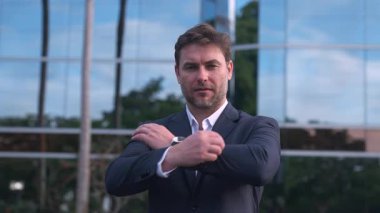 İşletme yöneticisi modern cam ofis binasının önünde kollarını kavuşturmuş poz veriyor. Takım elbiseli yetişkin adam liderlik, güven ve kurumsal başarıyı temsil ediyor. Sahne iş gücünü ve otoriteyi gösteriyor