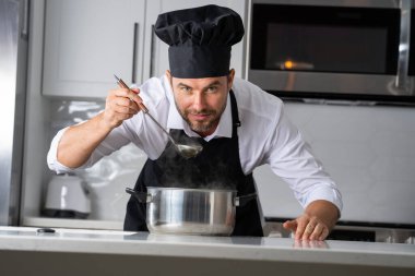 Profesyonel üniformalı modern şef. Kaşıkla tencereye çorba karıştıran erkek aşçının eline yakın plan. Yemek pişirme, aşçılık ve insan konsepti - erkek aşçı tencereli veya tencereli.