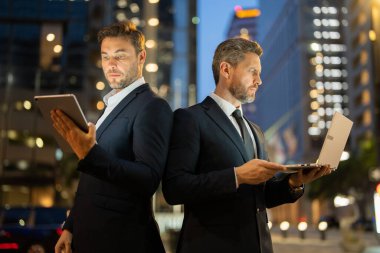 İki işadamı arka arkaya gece New York 'ta tablet ve dizüstü bilgisayardaki verileri analiz ediyor. Erkek profesyoneller rekabet ve kararlılığı yansıtır. Sahne teknolojiyi, iş odaklarını ve kentselliği vurguluyor