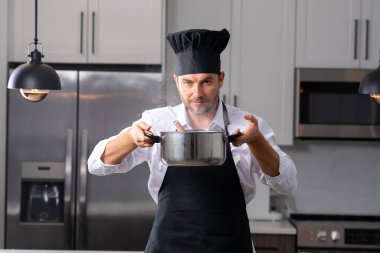 Profesyonel üniformalı modern şef. Kaşıkla tencereye çorba karıştıran erkek aşçının eline yakın plan. Yemek pişirme, aşçılık ve insan konsepti - erkek aşçı tencereli veya tencereli.