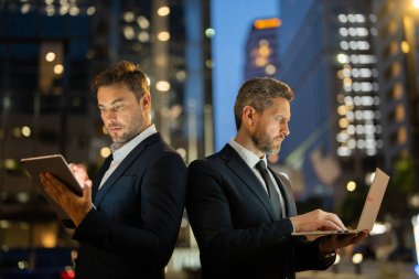 İki işadamı arka arkaya gece New York 'ta tablet ve dizüstü bilgisayardaki verileri analiz ediyor. Erkek profesyoneller rekabet ve kararlılığı yansıtır. Sahne teknolojiyi, iş odaklarını ve kentselliği vurguluyor