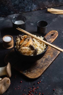 Noodles with eringi mushrooms in a black plate
