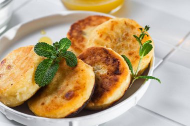 syrniki with honey on a white plate