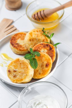 syrniki with honey on a white plate