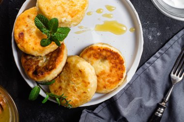 syrniki with honey on a white plate