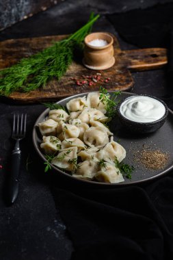 Ekşi kremalı hamur tatlısı ve siyah tabakta otlar. Etli börek.